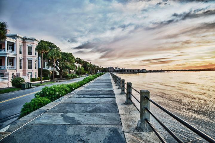 Seaside walkway lined with palm trees and historic buildings at sunset.