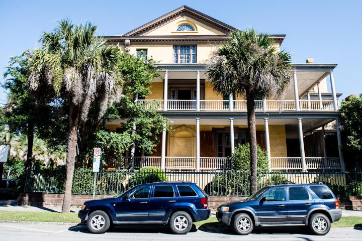 Two SUVs parked in front of a large yellow house with palm trees.