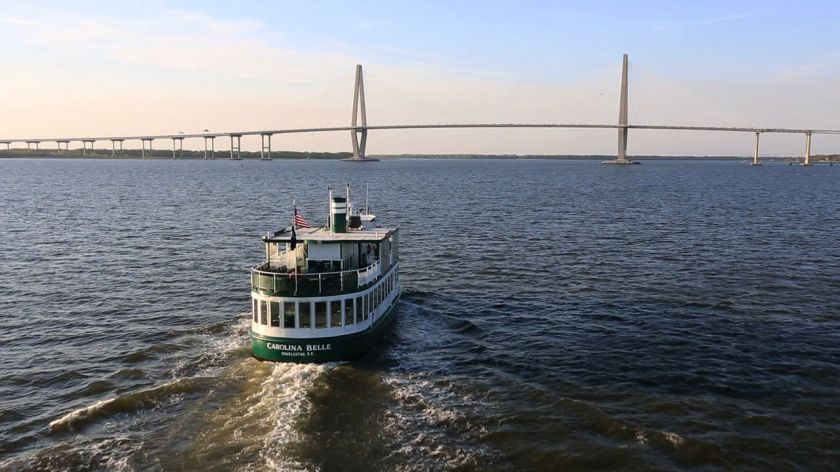 Boat on water with long suspension bridge in background under clear sky.